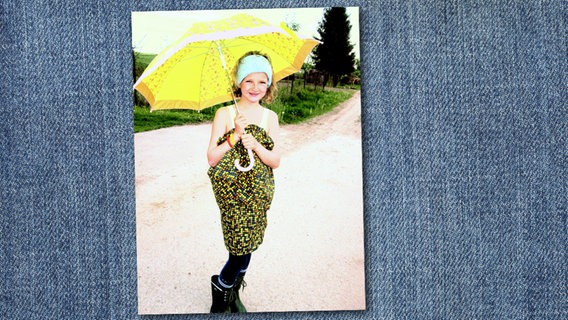 Ein Mädchen in einem selbstgenähten Kleid in Gelb- und Brauntönen mit passendem Schirm.  Foto: Familie Ohly