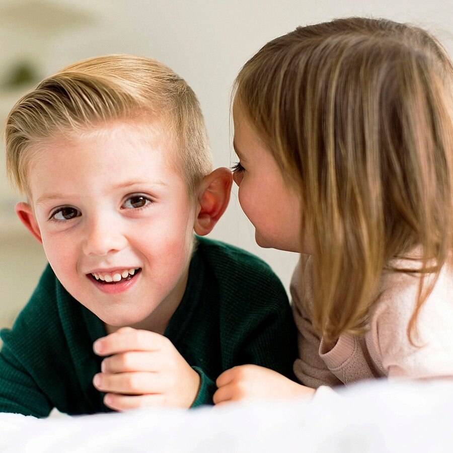 Zwei Kinder flüstern sich im Bett liegend etwas zu. © Bildagentur-online/Tetra Images 