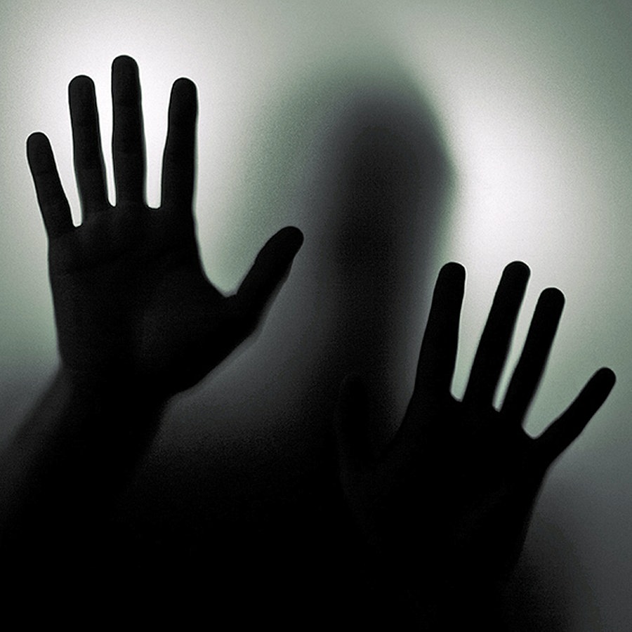 Eine dunkle Silhouette mit vorgehaltenen Handflächen hinter einer Glasscheibe. © fotolia.com Foto: Jakub Krechowicz