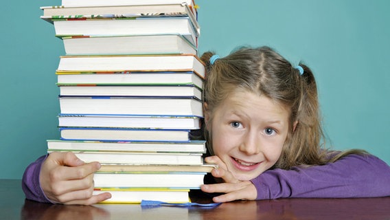 Ein Mädchen umgreift einen hohen Stapel mit Büchern. © fotolia.com Foto: photophonie
