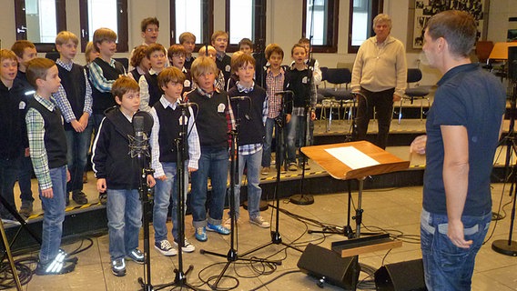 Ein Jungen-Chor steht in einem Studio, im Hintergrund ist  Rolf Zuckowski -Kinderliedermacher- zu sehen. © NDR Foto: Svenja Müller