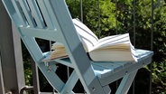 Ein Buch liegt auf einem Stuhl auf einem Balkon. © NDR Foto: Katharina Mahrenholtz