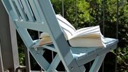 Ein Buch liegt auf einem Stuhl auf einem Balkon. © NDR Foto: Katharina Mahrenholtz