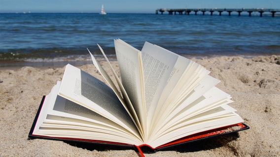 Ein Buch liegt aufgeschlagen am Strand, im Hintergrund die Ostsee. © Katharina Mahrenholtz Foto: Katharina Mahrenholtz