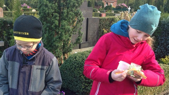 Zwei Kinder auf einem Friedhof, das Mädchen hält ein Glas mit Bärlauchbutter in der Hand. © NDR Foto: Beke Schulmann