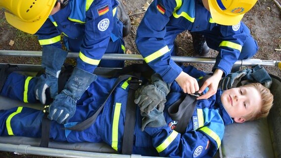 Bei einer Übung des THW wird ein Kind von Helfern auf einer Tragbahre mit Gurten gesichert. © NDR Foto: Lenne Kaffka