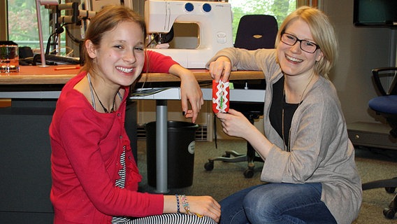 Studiogast Elli und Moderatorin Jessica knien vor dem Studiotisch, auf dem eine Nähmaschine steht und posieren mit einem rot-weiß-gepunkteten Taschentüchertäschchen. © NDR Foto: Florian Jacobsen