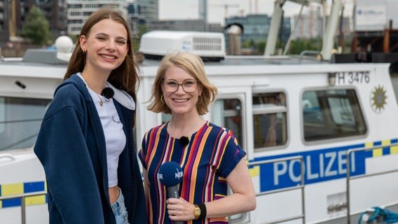 Das ehemalige Pfefferkorn Alice (Emilia Flint) mit NDR Moderatorin Jessica Schlage Emilia Flint und Jessica Schlage stehen im Hafen vor einem Boot der Wasserschutzpolizei. © NDR Foto: Aaron Moser