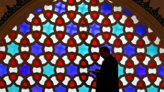 Die Silhouette eines lesenden Mannes ist vor einem bunten Fenster der Sehitlik-Moschee am Mittwoch in Berlin zu sehen. © dpa - picture-alliance 