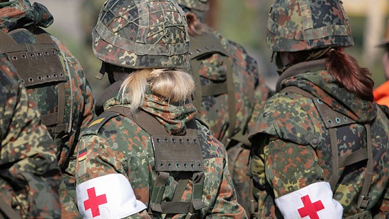 Zur Befehlsausgabe voll ausgerüstete angetretene Sanitäter. Rücken zur Kamera. Am Arm eine Binde mit dem Rot-Kreuz-Schutzzeichen. © Bundeswehr/B.Wilke Foto: Wilke