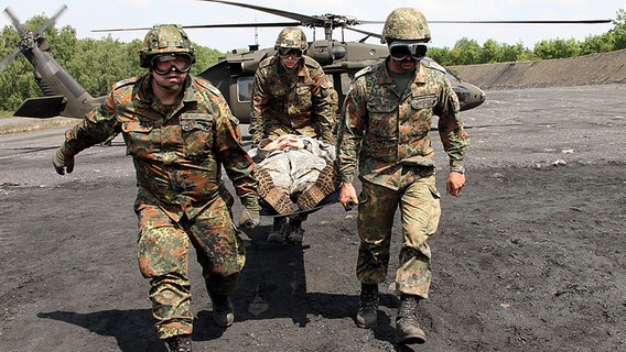 Drei Soldaten transportieren einen auf einer Trage liegenden Verwundeten aus einem Hubschrauber. © Bundeswehr/Bienert Foto: Bienert