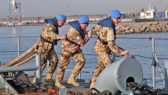 Drei Soldaten mit blauem Barett ziehen auf einer Fregatte ein dickes Tau um das Schiff festzumachen. © © Bundeswehr/Fischer Foto: Fischer