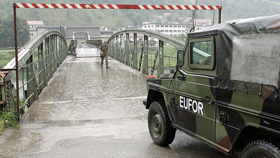 Vor einer Brücke hält ein Militärfahrzeug mit der Aufschrift EUFOR. Ein Soldat erkundet die Brücke. © Bundeswehr/Lars Pötzsch ©  ©Bundeswehr/Lars Pötzsch Foto: Lars Pötzsch