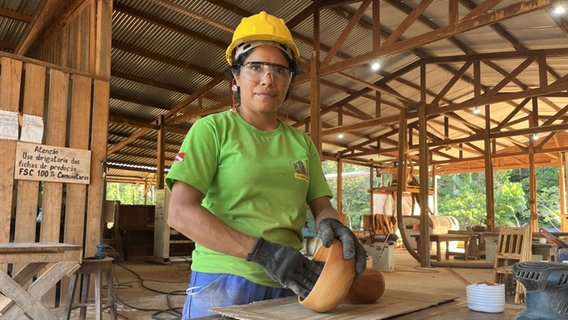 Eine Frau mit gelbem Helm und grünem T-Shirt bearbeitet ein Holzobjekt © NDR Foto: Tom Noga