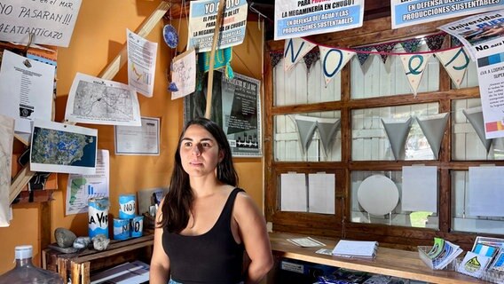 Eine jüngere Frau mit dunklen langen Haaren steht in einem Büro voller Material mit Aufschrift auf Spanisch "No a la mina" (Nein zur Mine) in Argentinien © NDR Foto: Max-Marian Unger