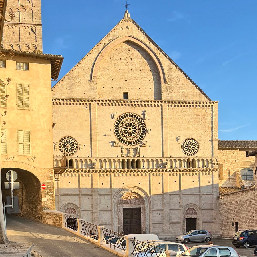 Eine Kirche in Assisi (Italien) im Sonnenlicht, daneben eine Straße und vor der Kirche einige parkende Autos © NDR Foto: Peter Kaiser
