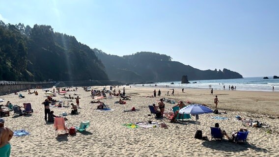 Playa de Aguilar, Strand an der Atlantikküste Menschen, die sich am Strand sonnen, im Hintergrund sind Berge zu erkennen © NDR Foto: Carsten Vick