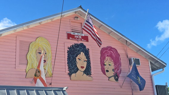 Drei Frauenköpfe sind gemalt auf eine rosa Fassade mit US-Fahne in den Florida Keys © NDR Foto: Mareike Aden