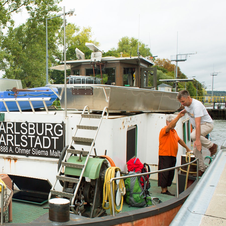 Ein Mann in heller Kleidung spricht mit einem Kapitän auf einem Binnenschiff an der Schleuse © Fabian Zapatka Foto: Fabian Zapatka