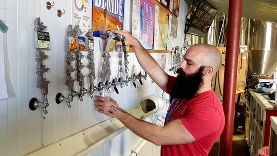 Ein Mann mit langem Bart zapft Bier aus einem der vielen Hähne an der Wand in Fort Worth, USA © NDR Foto: Guido Meyer