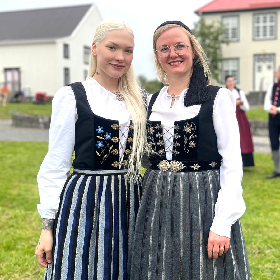 Zwei lächelnde Frauen stehen im Vordergrund in isländischen Trachten, dahinter sind weitere Menschen und zwei Gebäude unscharf zu erkennen © NDR Foto: Max-Marian Unger