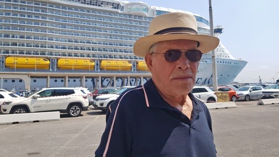 Ein älterer Mann mit Hut vor einem Kreuzfahrtschiff © NDR Foto: Thomas Becker