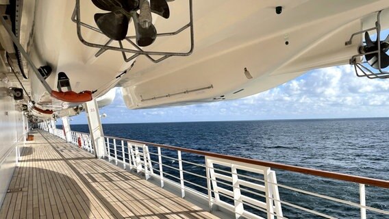 Ein Beiboot hängt an Deck eines Keuzfahrtschiffs, dahinter das Meer © NDR Foto: Dennis Burk und Julia Küppers  