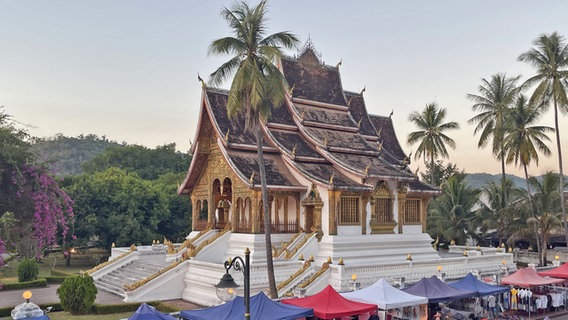 Ein Tempel in Laos, umgeben von bunten Zelten © NDR Foto: Dennis Burk