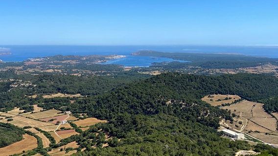 Blick aus Vogelperspektive auf die felsige-grüne Landschaft von Menorca - im Hintergrund das Meer. © NDR Foto: Carsten Vick