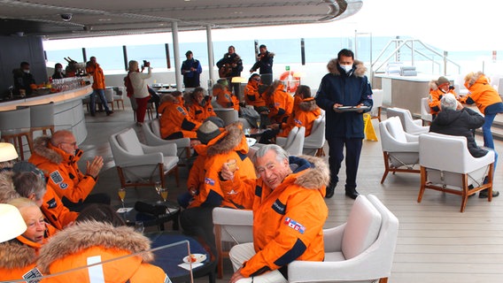 Menschen in warmen Outfits sitzen draußen auf einer Outdoorbaar auf der Kreuzfahrt-Yacht Commandant Charcot in der Arktis © NDR Foto: Sven Weniger