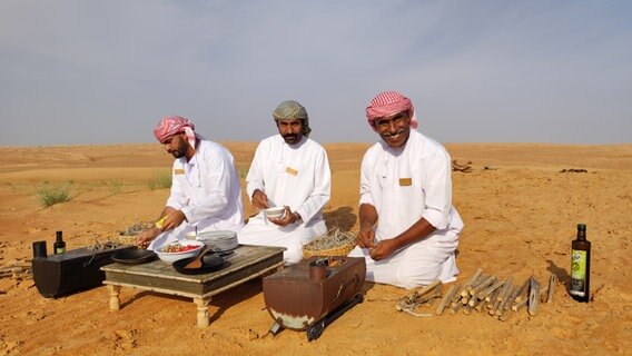 Drei Männer in weißen Gewändern bereiten Essen in der Wüste im Oman zu. © NDR Foto: Isa Hoffinger