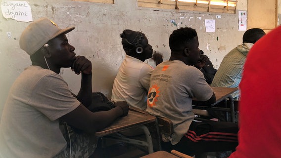 Mehrere Schüler sitzen im Senegal in einem Klassenraum an Tischen. © NDR Foto: Barbara Schmickler