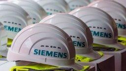 aufgereihte weiße Schutzhelme mit der Aufschrift "Siemens", darunter jeweils eine gefaltete gelbe Warnweste © dpa Bildfunk Foto: Jens Büttner