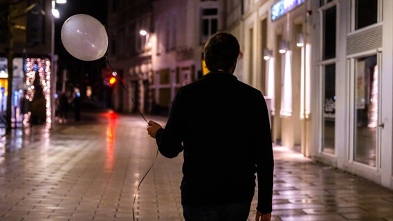 Ein Mann mit einem Luftballon in der Hand spaziert in der Silvesternacht alleine durch die leere Oldenburger Fußgängerzone © dpa-Bildfunk Foto: Mohssen Assanimoghaddam