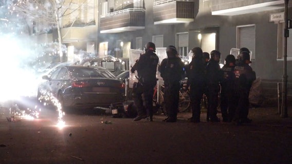Polizeibeamte stehen in Berlin hinter explodierendem Feuerwerk auf einer Straße. © Julius-Christian Schreiner/TNN/dpa 