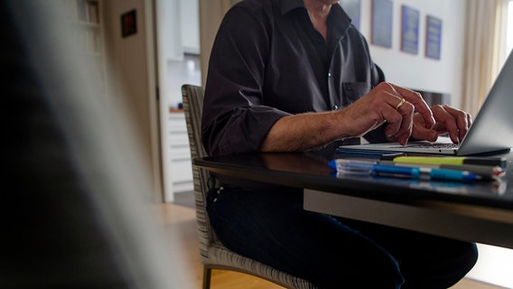Ein Mann sitzt zuhause an einem Esstisch und arbeitet an einem Laptop. © dpa 