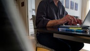 Ein Mann sitzt zuhause an einem Esstisch und arbeitet an einem Laptop. © dpa 