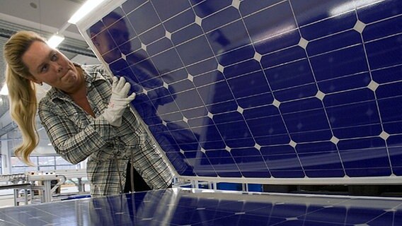 Eine Mitarbeiterin der Centrosolar Sonnenstromfabrik GmbH Wismar hebt eine Solarzellenplatte hoch. © dpa Foto: Jens Büttner