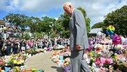 König Charles III. sieht sich die Blumen und Ehrungen vor dem Rathaus an, bevor er sich mit Mitgliedern der Gemeinde Southport trifft. © Paul Ellis/PA Wire/dpa 