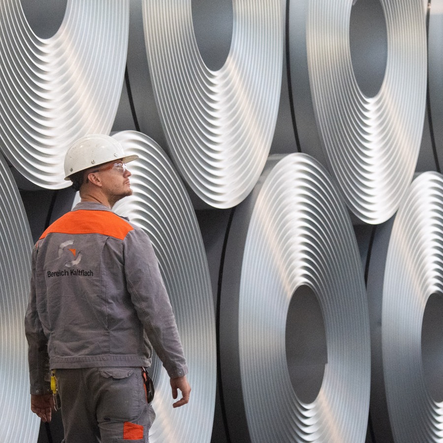 Eine Mitarbeiter geht bei der Salzgitter AG an aufgewickeltem Stahl (Coils) vorbei © picture alliance/dpa Foto: Julian Stratenschulte