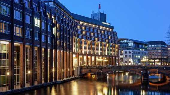 Zu sehen ist das Steigenberger Hotel in der Hamburger Innenstadt. Es hat eine Rotklinker-Fassade und liegt an einem Fleet. Es ist hier in einer Nachtaufnahme zu sehen und schön beleuchtet. © Steigenberger 