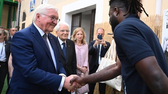 Bundespräsident Frank-Walter Steinmeier schüttelt einem Geflüchteten in Italien die Hand. © Britta Pedersen/dpa 