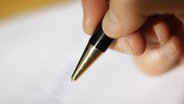 Eine Hand hält einen Stift und schreibt etwas auf ein Blatt Papier. © dpa picture alliance Foto: Ina Fassbender