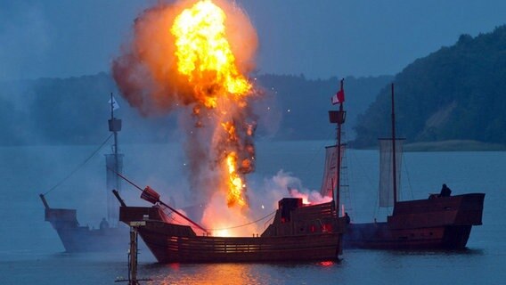 Eine Kogge der Störtebeker-Festspiele fährt durch einen Feuerball vor der Naturbühne Ralswiek. © dpa Bildfunk 