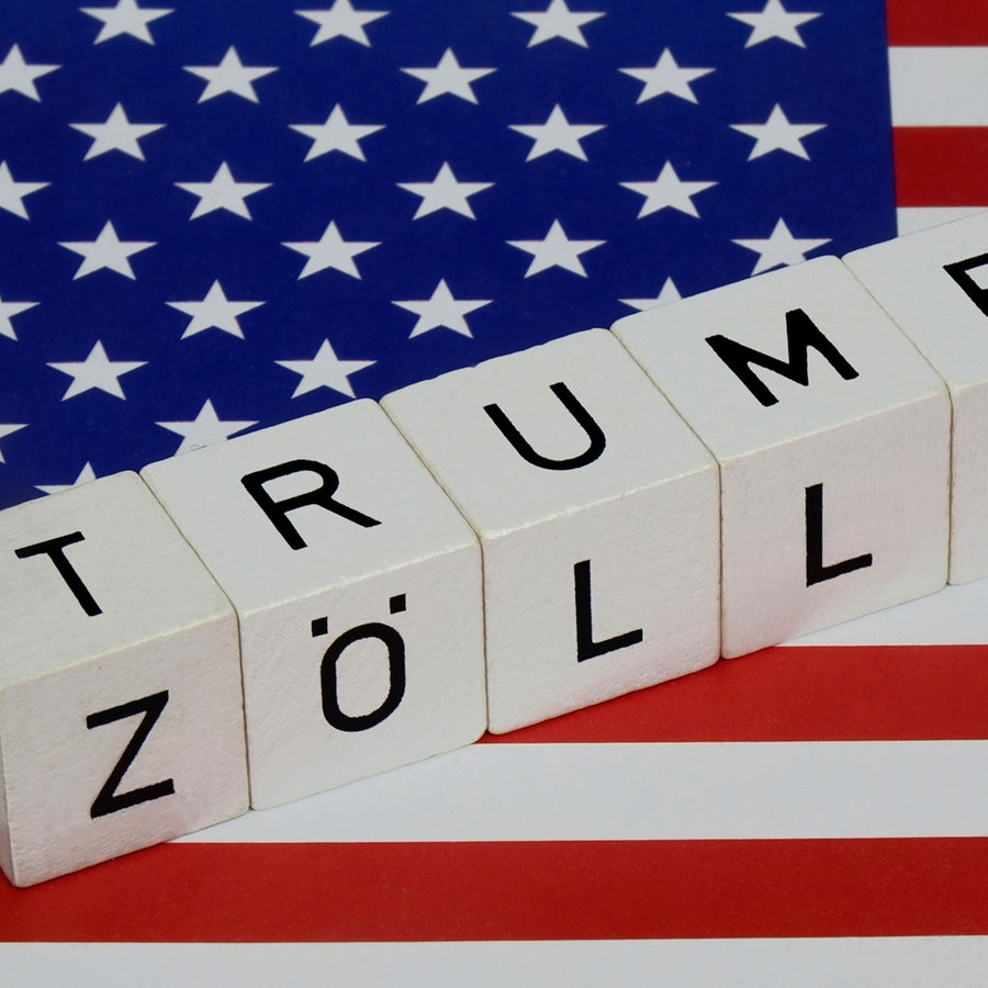 Auf einer USA Fahne befinden sich Buchstabenwürfel mit den Schriftzügen Trump und Zölle. © picture alliance / ZB Foto: Sascha Steinach