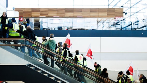 Mitarbeiter der der Unternehmenssparte Lufthana Technik demonstrieren mit Fahnen in der Abflughalle im Terminal 1 des Flughafens BER. © Carsten Koall/dpa 
