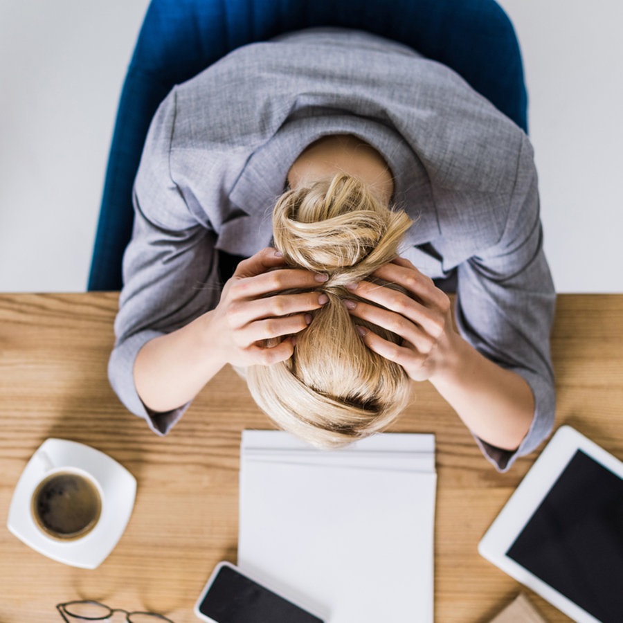 Eine Frau am Schreibtisch von oben, die erschöpft die Hände über den Kopf legt. © Colourbox Foto: #246329