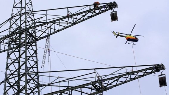 Ein Helikopter zieht bei Gudow an der Autobahn A 24 ein Vorseil von einem Starkstrommast zum nächsten. Ein Helikopter zieht bei Gudow an der Autobahn A 24 ein Vorseil von einem Starkstrommast zum nächsten. © dpa-Bildfunk Foto: Jens Büttner