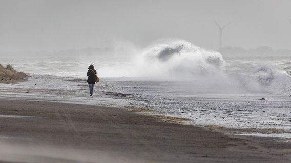 Eine Frau kämpft während eines Sturmtiefs am Strand gegen den Wind. © Imago Images/Priller&Maug Foto: Janis Meyer
