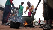 Menschen bereiten in einem Viertel von Khartum auf einer Straße Essen zu. © dpa-Bildfunk/AP 